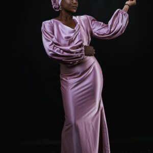 A young woman wearing a stylish pink silk dress and turban elegantly poses for a studio shoot.