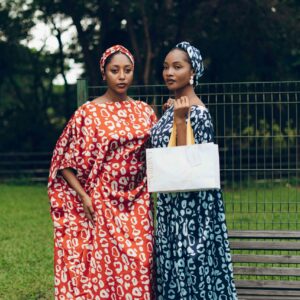 Two women in Nigerian traditional dresses pose gracefully outdoors, showcasing vibrant cultural fashion.